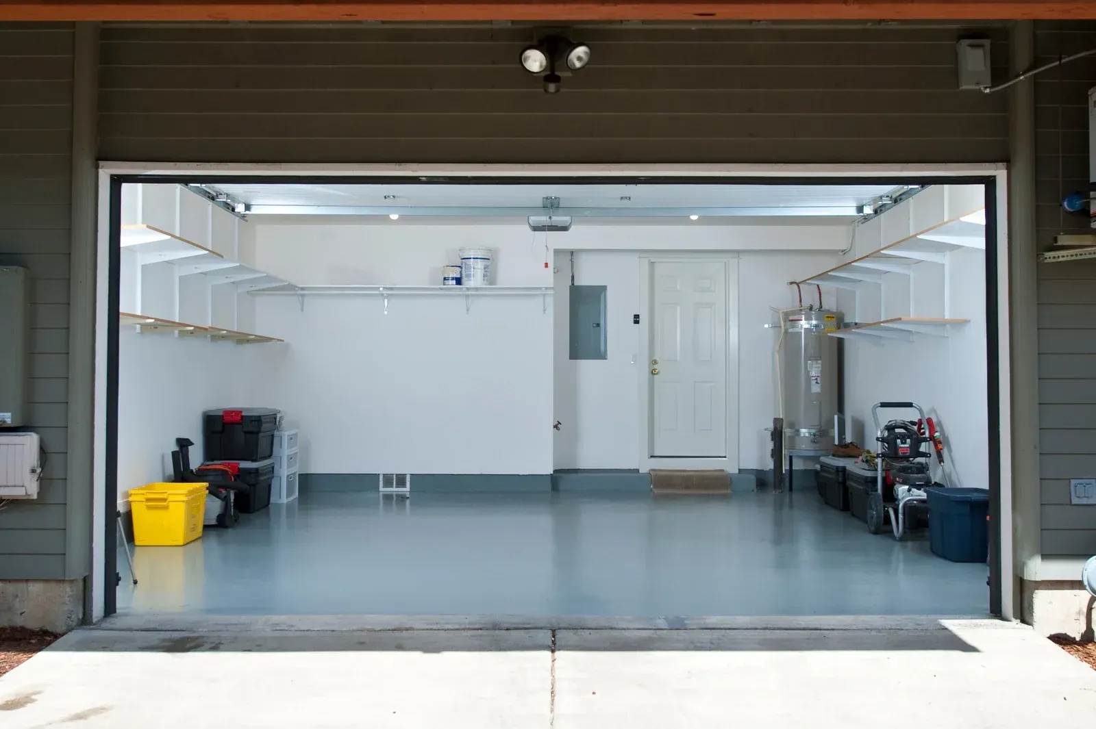 Garage interior, open door view. Gray floor, white walls and shelves, storage, door at back.