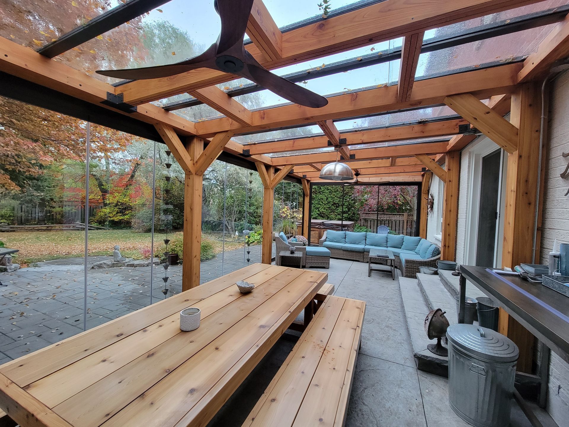 A wooden table and benches under a pergola with a ceiling fan.