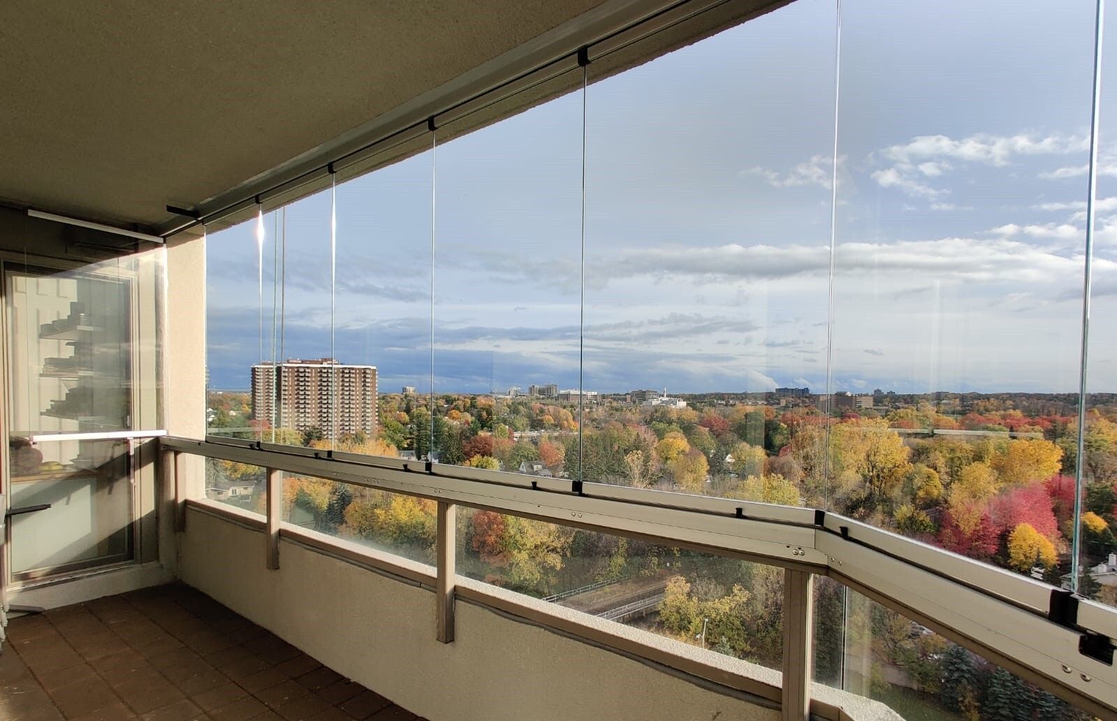 Balcony with clear glass panels, overlooking colorful autumn trees and cityscape.