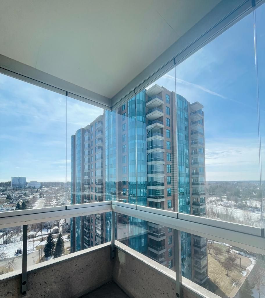 Glass-enclosed balcony overlooking a city with a tall, blue-tinted building.