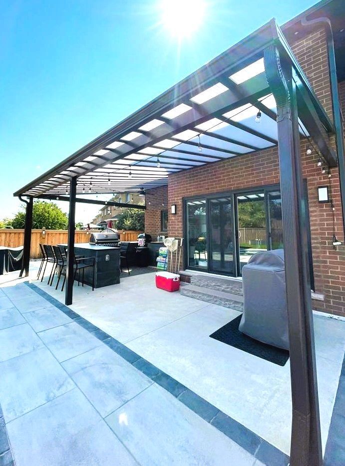 A patio with a pergola over it and a brick house in the background.