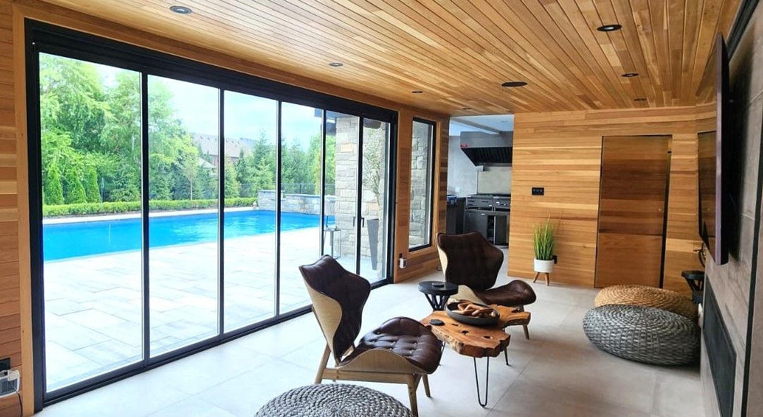 A living room with a lot of windows and a swimming pool in the background.