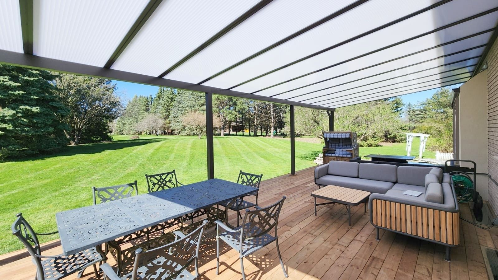 Patio with dining table and sofa under a covered roof, overlooking a grassy yard.