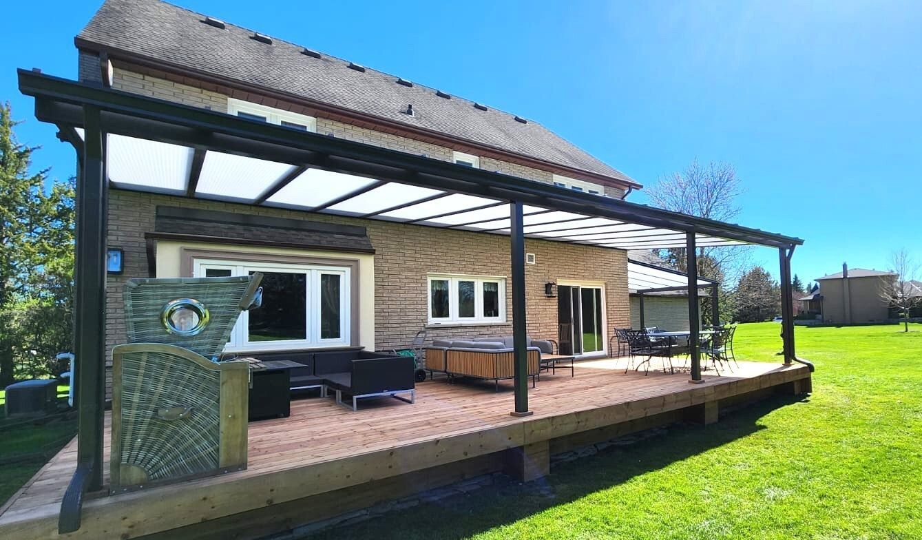 Backyard deck with a pergola, brick house, and green lawn on a sunny day.