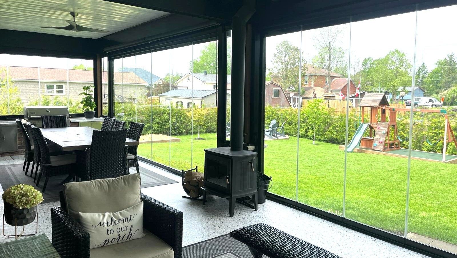 Sunroom with glass walls, outdoor furniture, fireplace, and a view of a green lawn with a play structure.