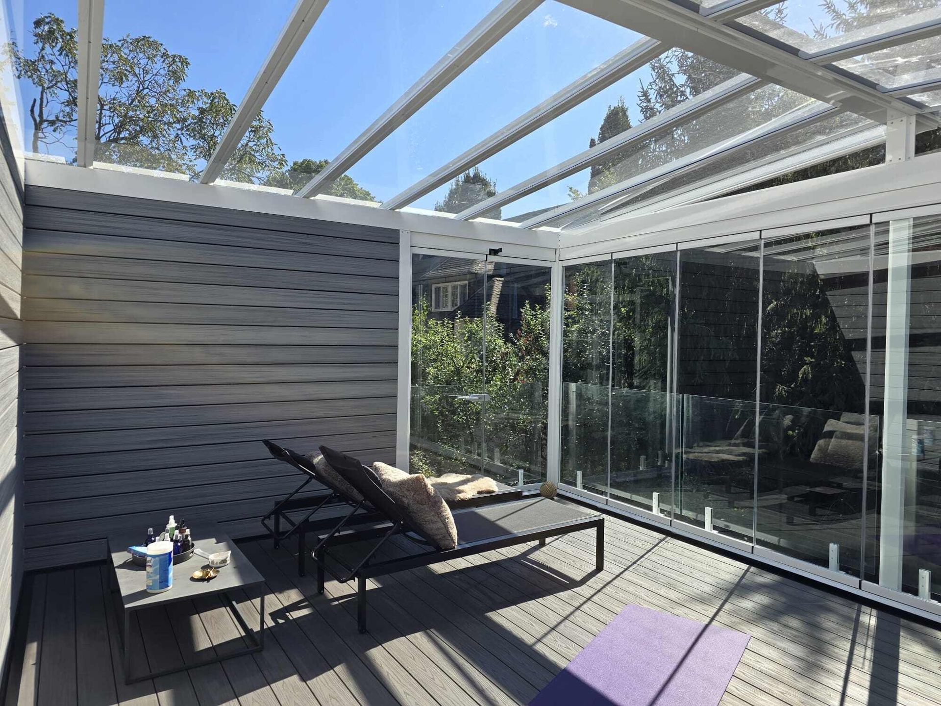 A deck with chairs and a table under a glass roof.