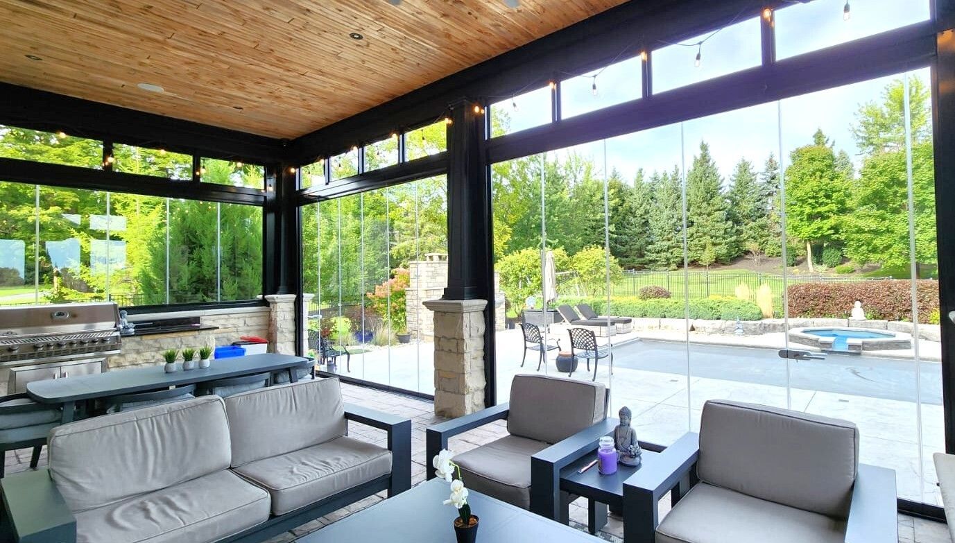 Modern building with dark gray exterior, large windows, and wooden accents. Sunny day, greenery in front.
