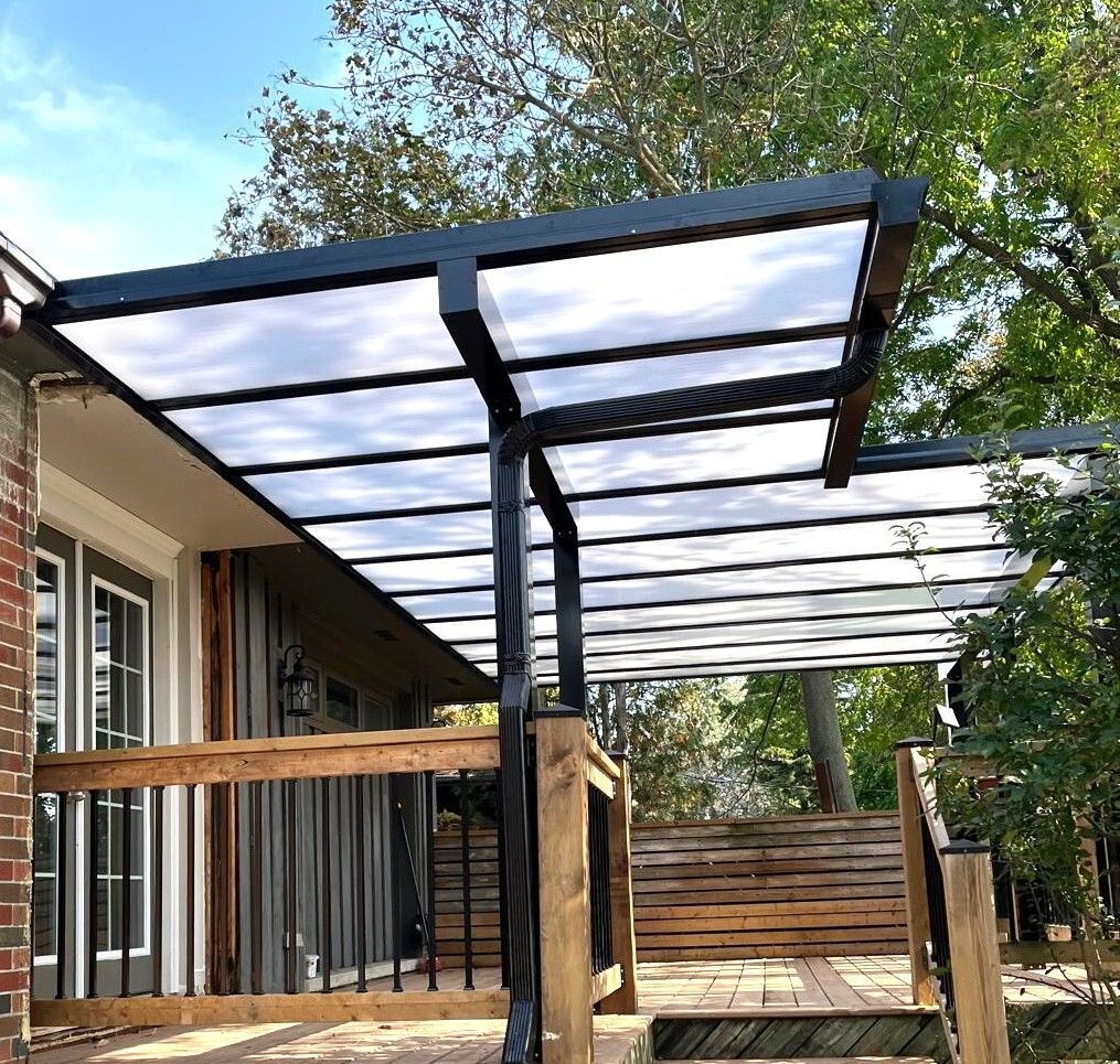 Black-framed patio cover with clear roof panels over a wooden deck, attached to a house.