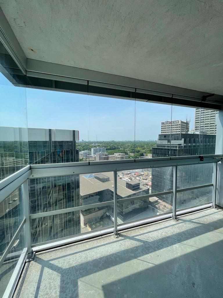 High-angle view from a balcony with glass railings overlooking city buildings and a blue sky.