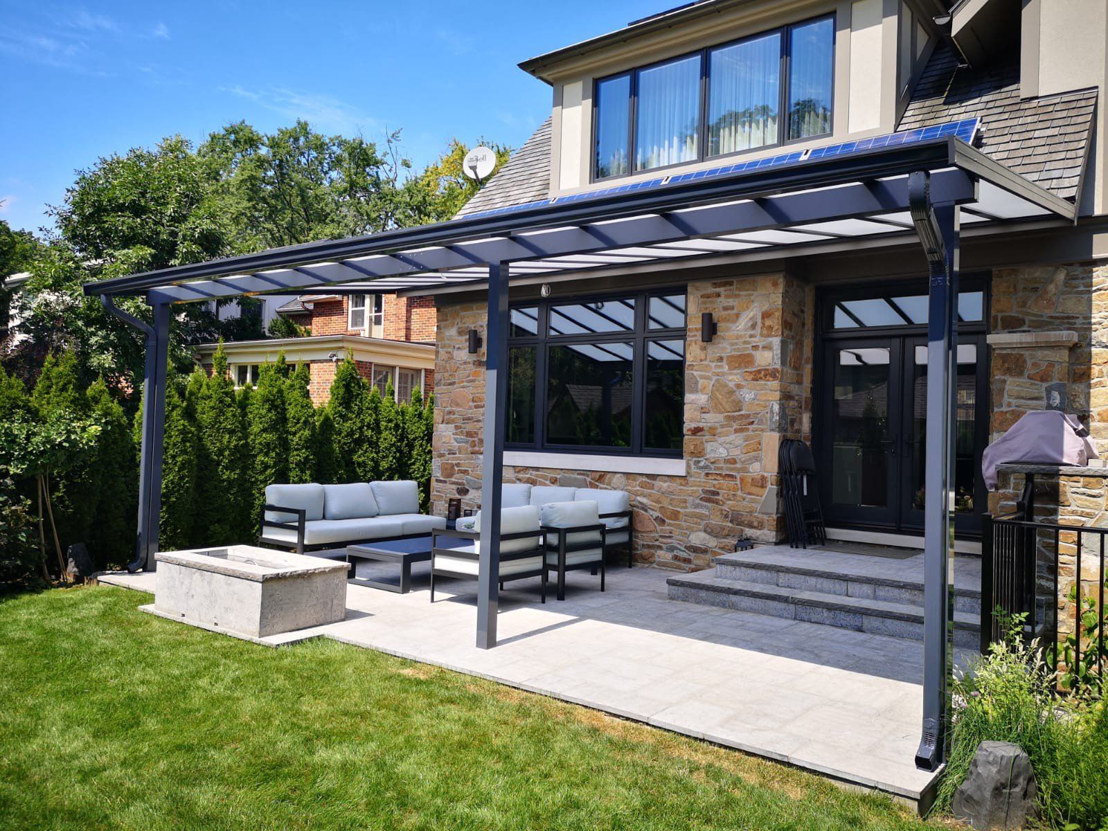 A patio with a pergola and a fire pit in front of a house.