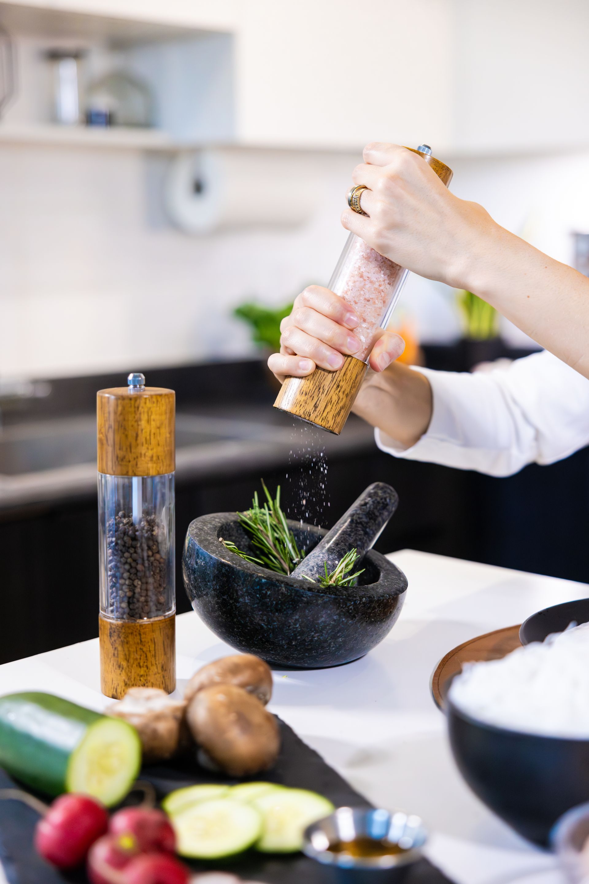 Hands grinding spices in a mortar and pestle beside chopped vegetables and cooking ingredients