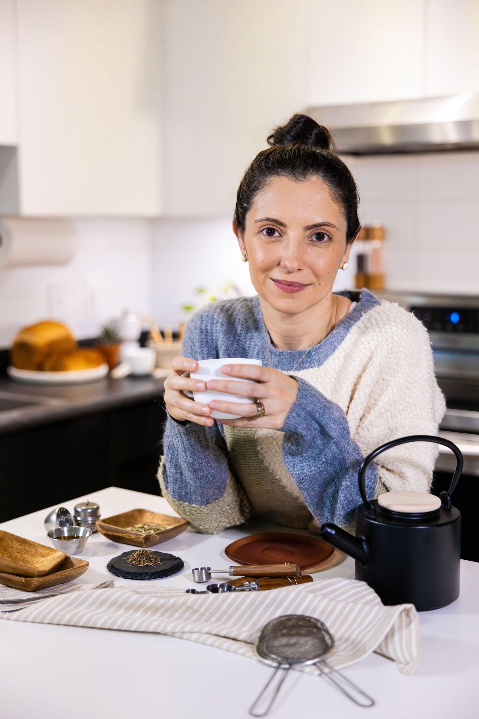 Person holding a mug at a kitchen counter with pastries, a kettle, and a plate of toast.