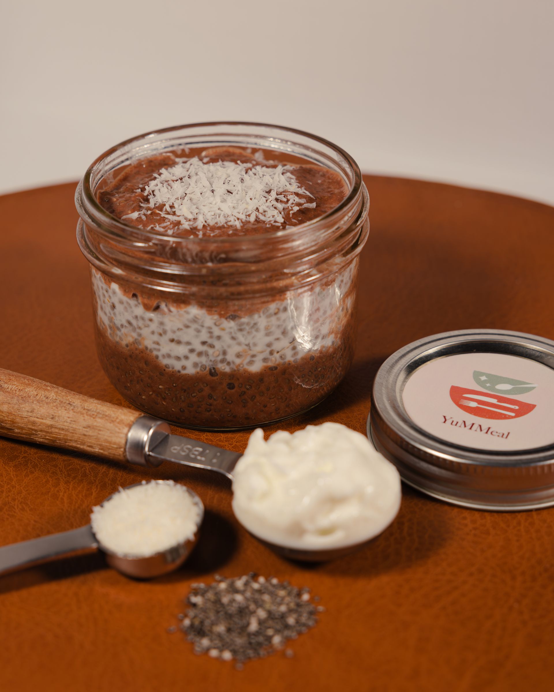 Jar of brown speckled scrub with spoon, cream, and lid on wooden table