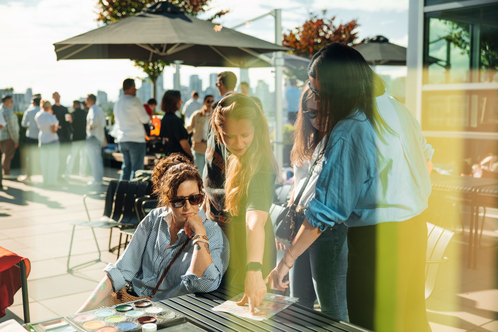 People chatting at an outdoor rooftop gathering under umbrellas, with a seated woman in the foreground.