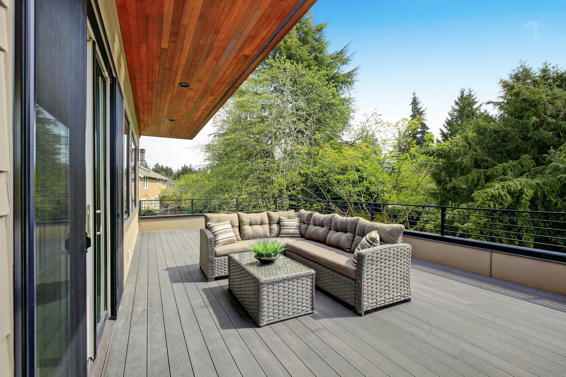 Outdoor deck with gray furniture, wood ceiling, surrounded by trees.