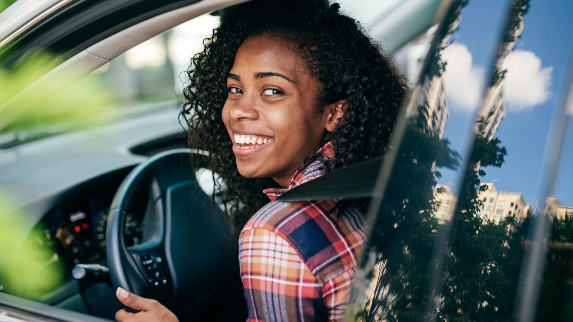 Smiling driver seated in a car, looking back over her shoulder through the open window.