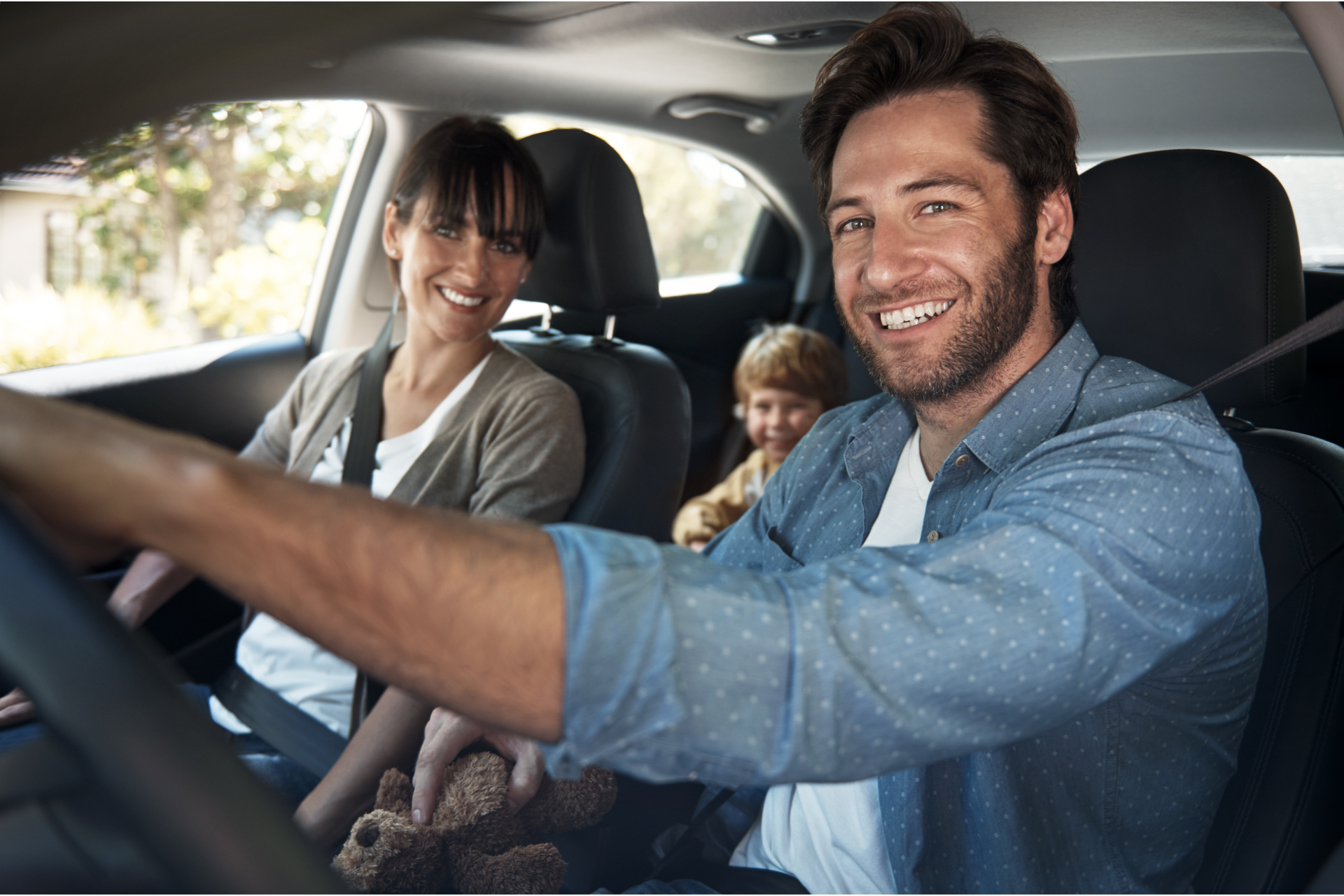 Smiling family riding in a car, with a driver and child in the back seat