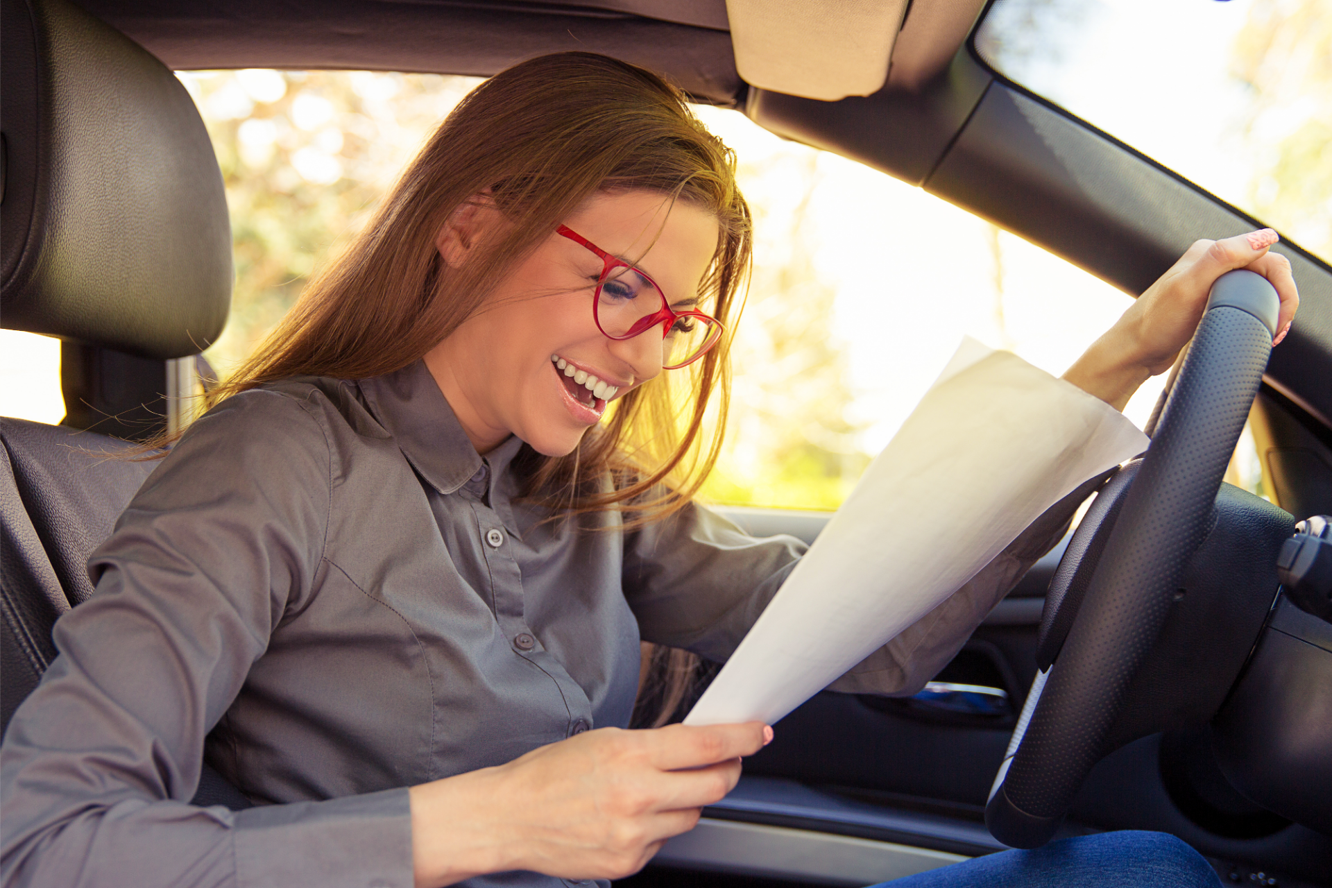 Smiling driver with glasses reading a paper inside a car