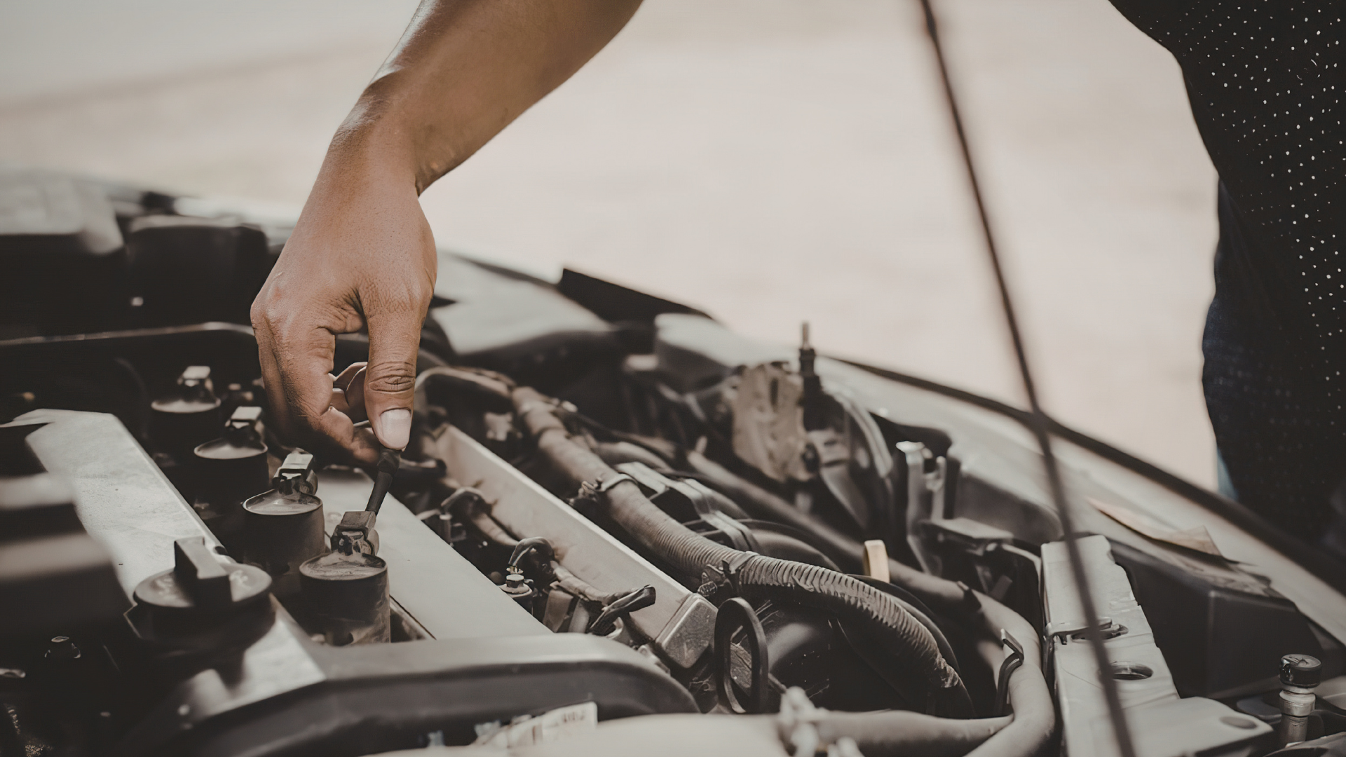A person’s hand reaching into an open car engine bay to perform maintenance.