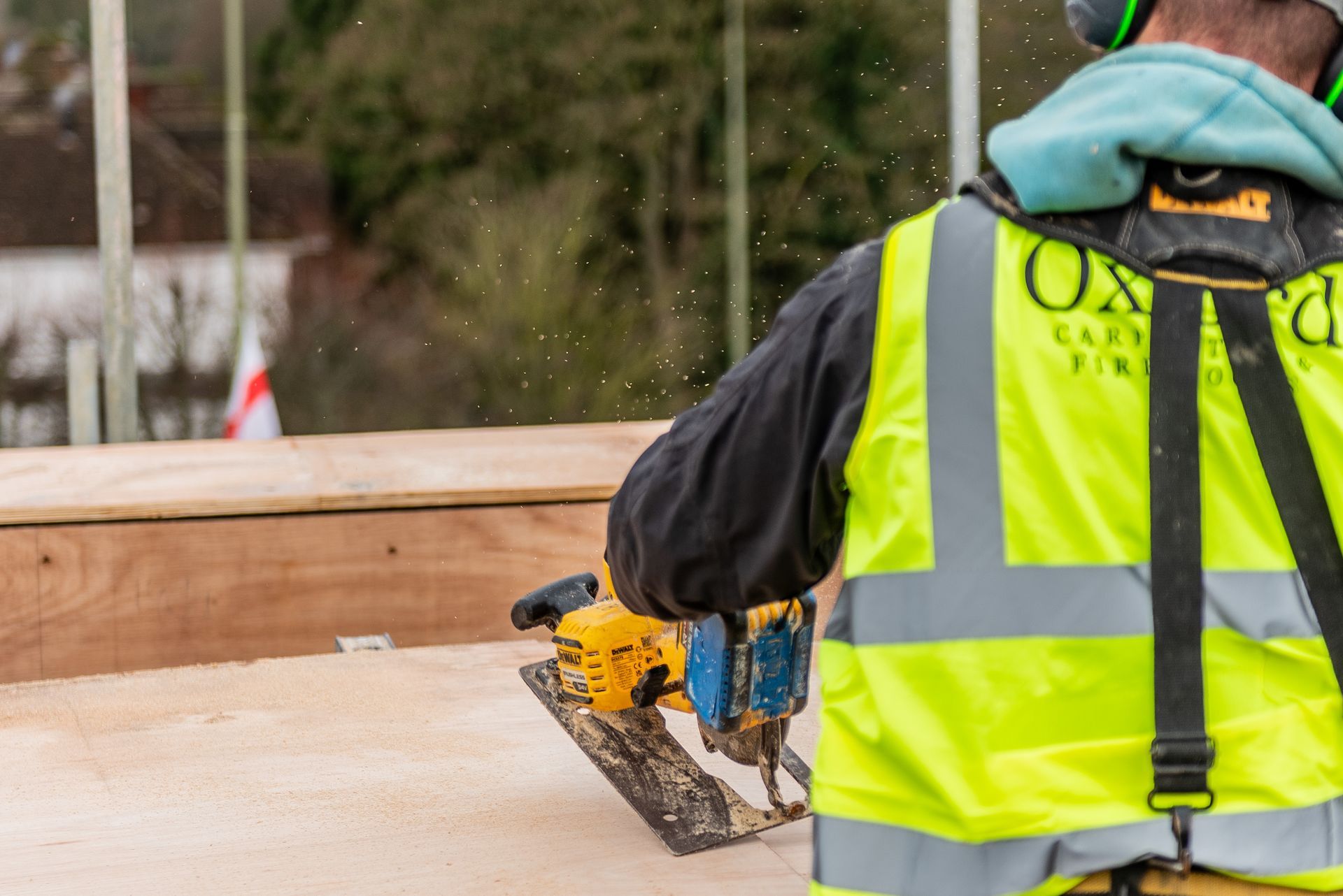 Construction worker using a saw, wearing a safety vest and ear protection.