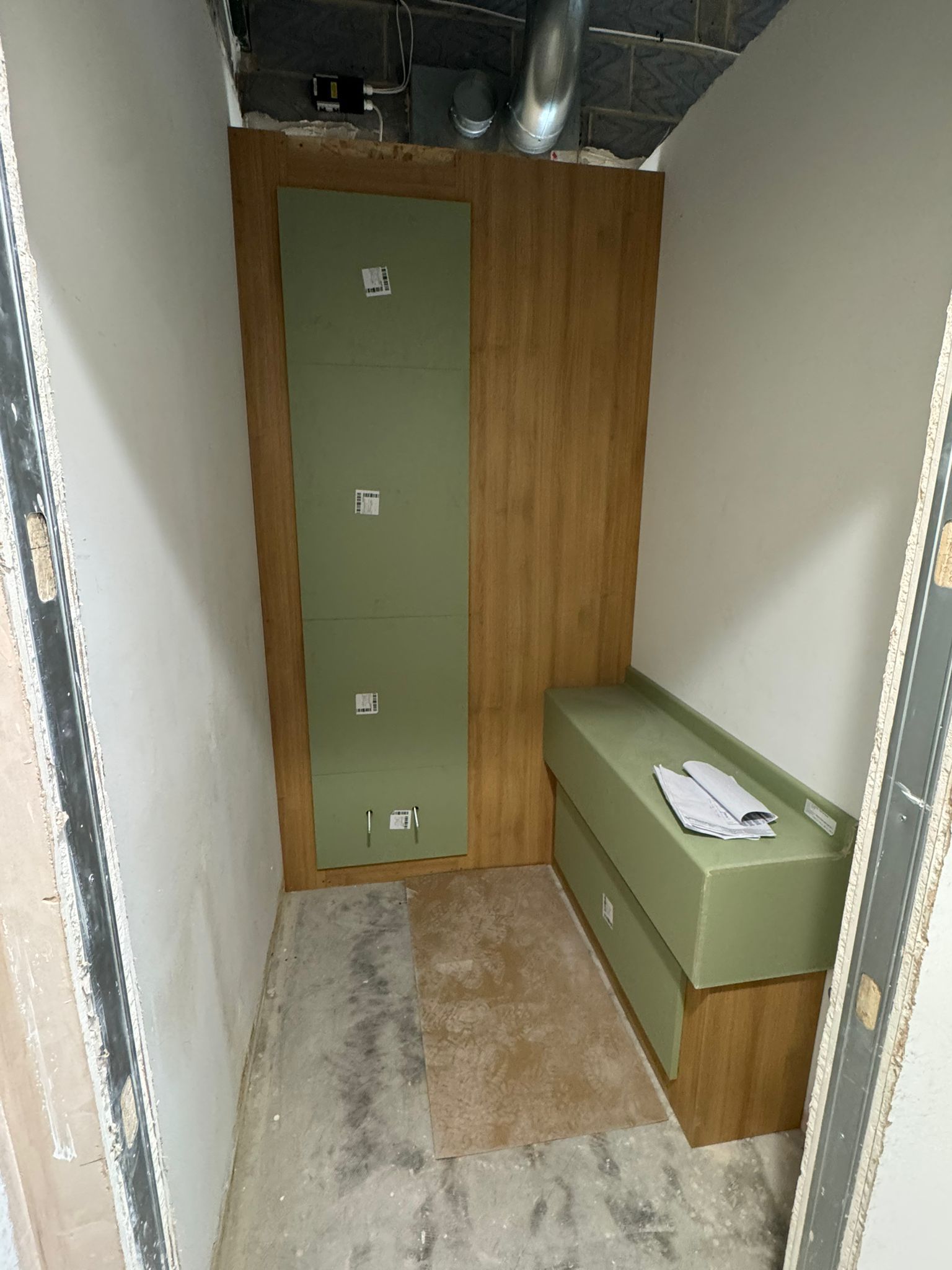 Interior space with unfinished walls, a wooden panel and green box-like furniture.