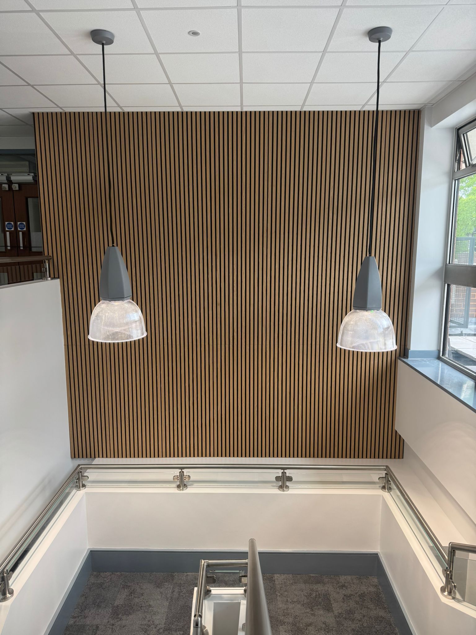 Wooden slat wall with two hanging lights above a stairwell.