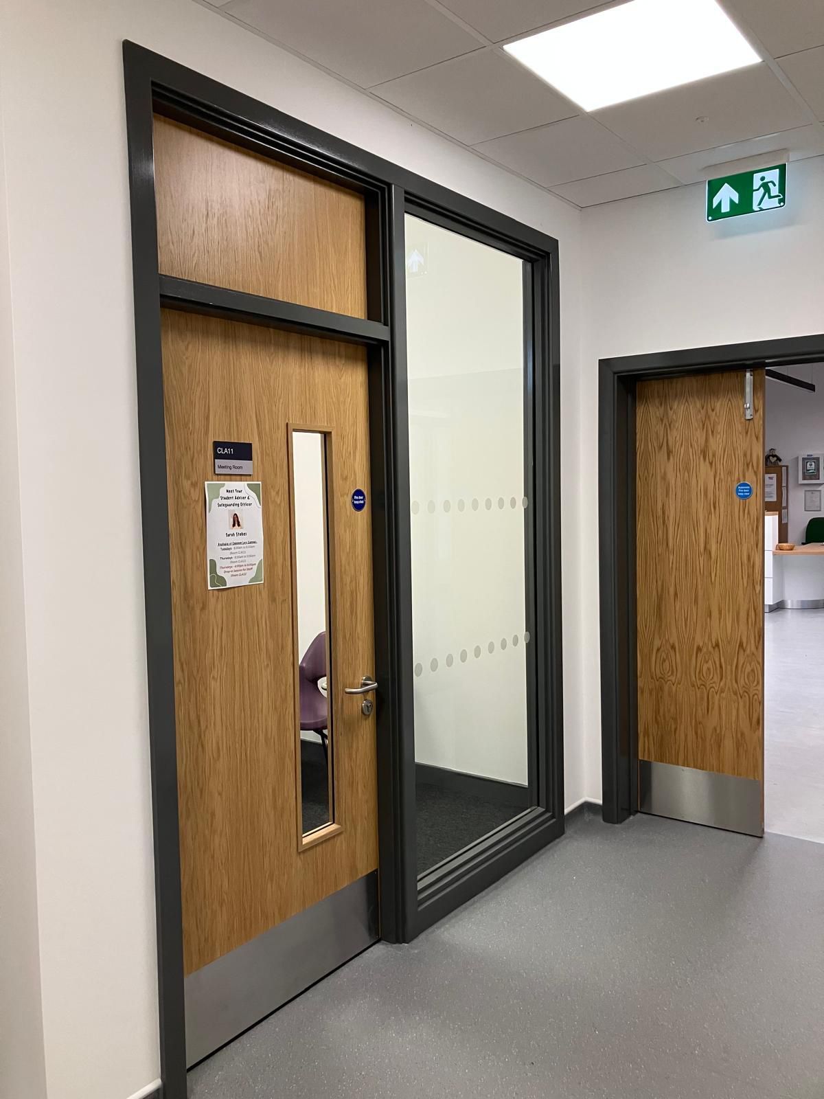 Two fire doors with dark frames, one with a glass panel, in a white hallway.