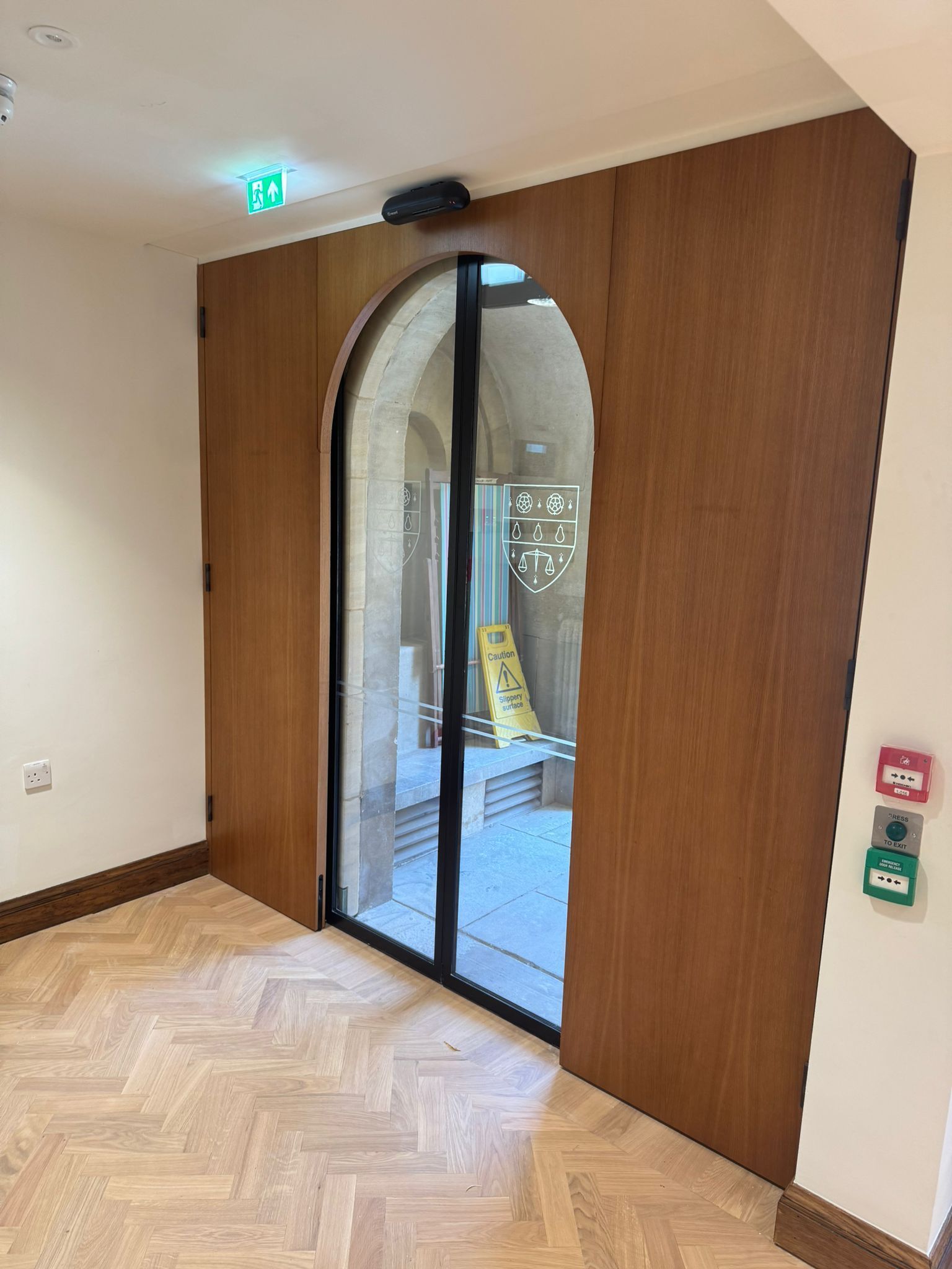 A fire door with an arched wooden wall. Emergency exit sign on the top.