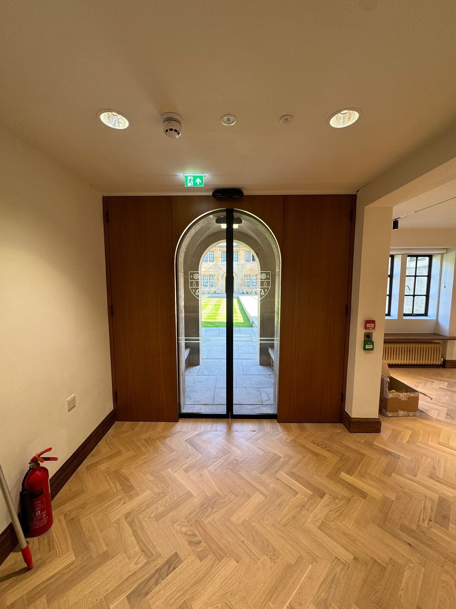 Fire door leading to a courtyard, inside view. Herringbone wood floor. Fire extinguisher and emergency exit sign visible.