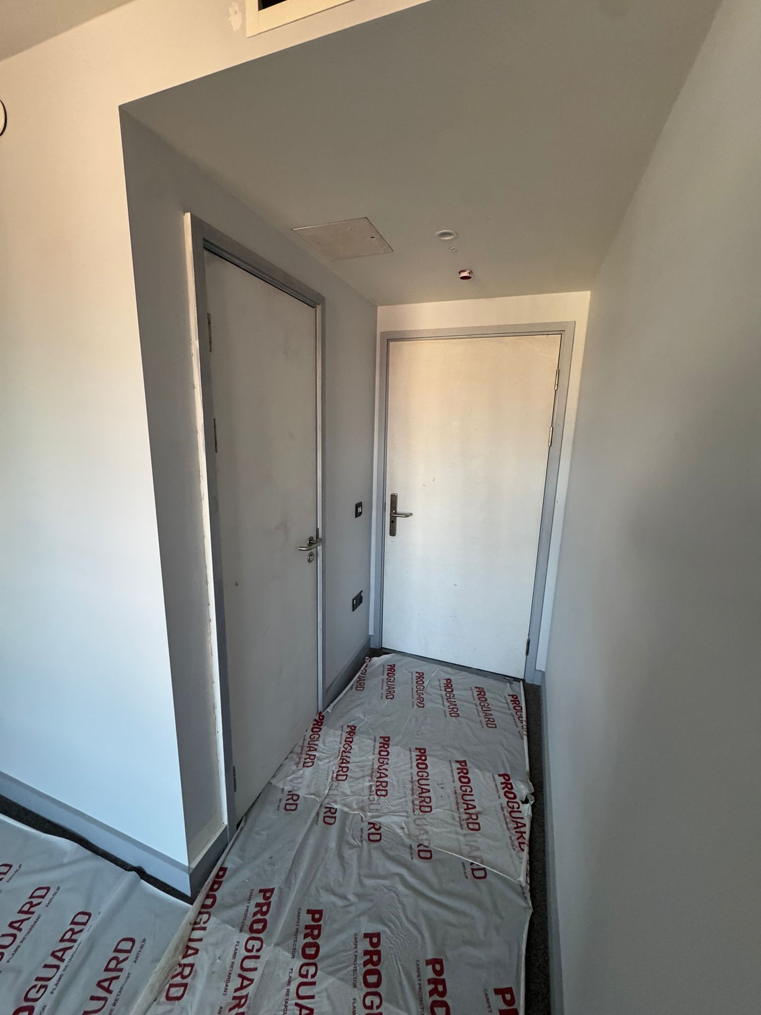 A person installing baseboard trim in a white room with a miter saw.