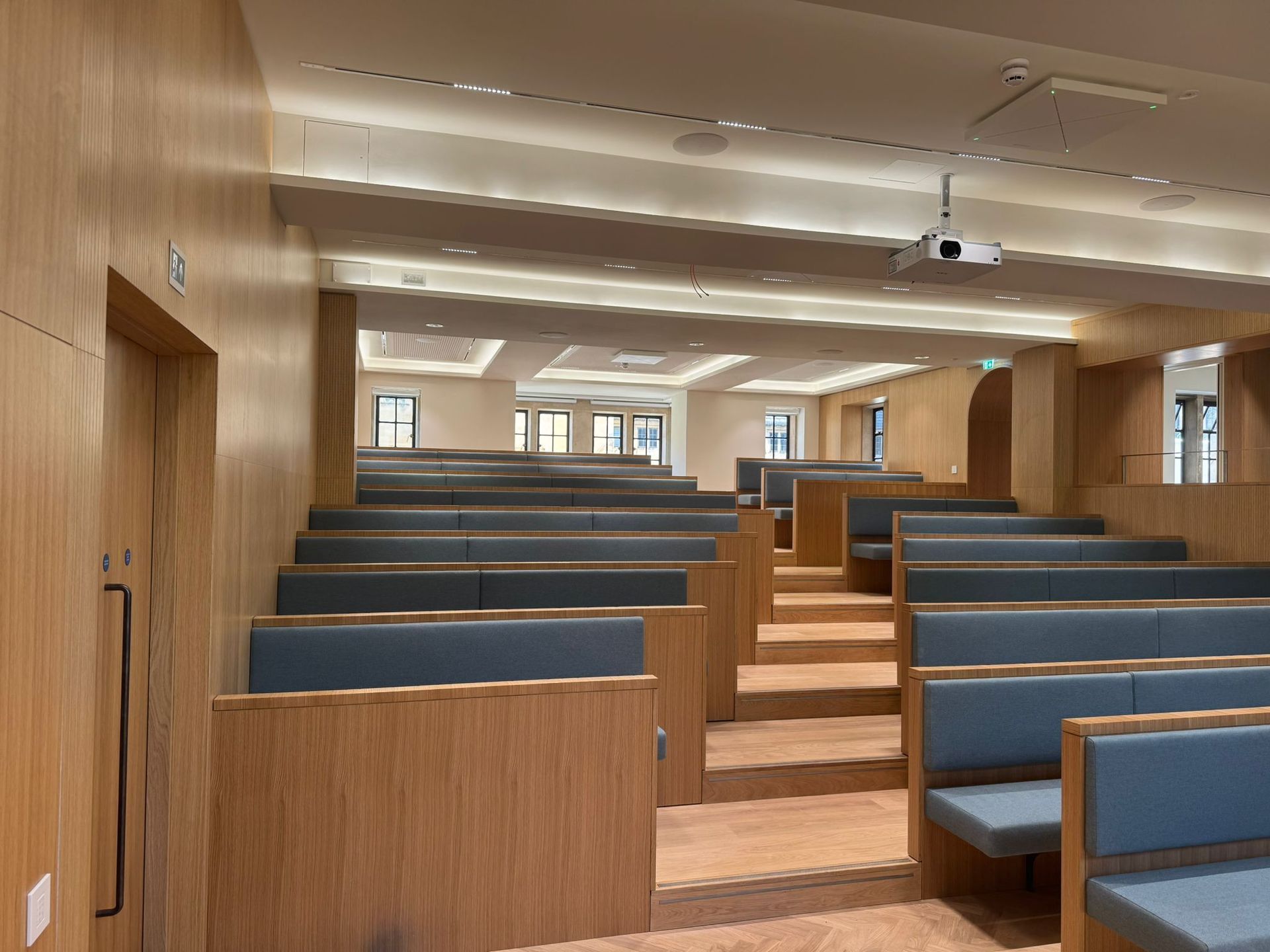 Lecture hall with tiered blue seating and light wood paneling.