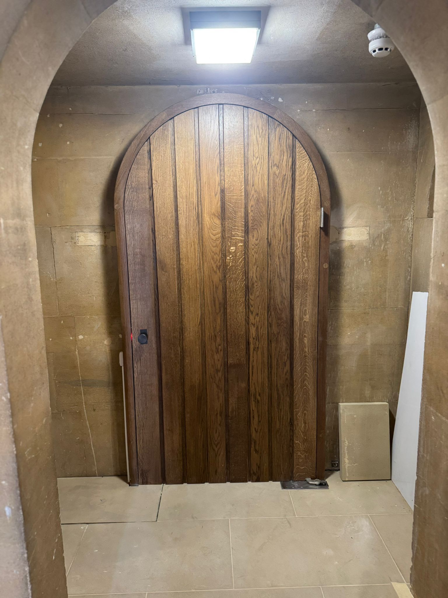 Wooden arched door in a stone-walled room, lit by an overhead light.