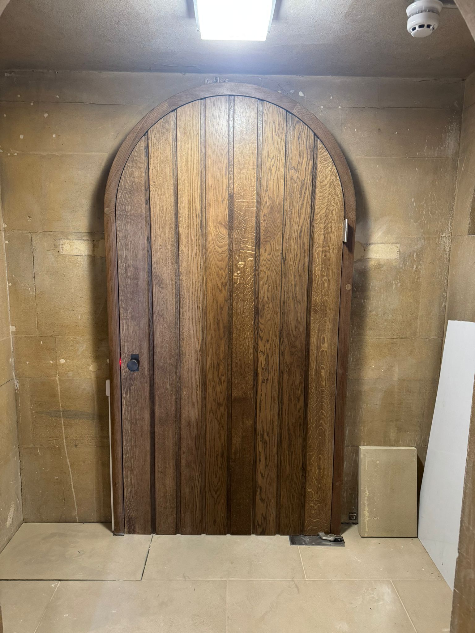 Wooden arched door in a stone-walled room, lit by an overhead light.