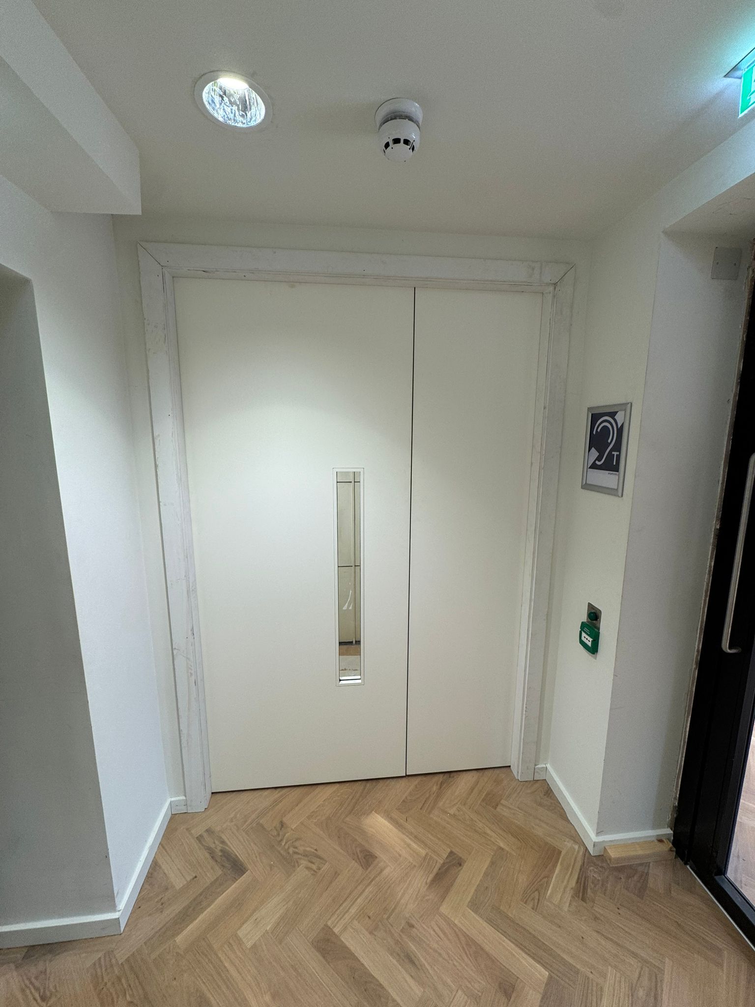 Double white doors with a rectangular window, surrounded by white walls. 