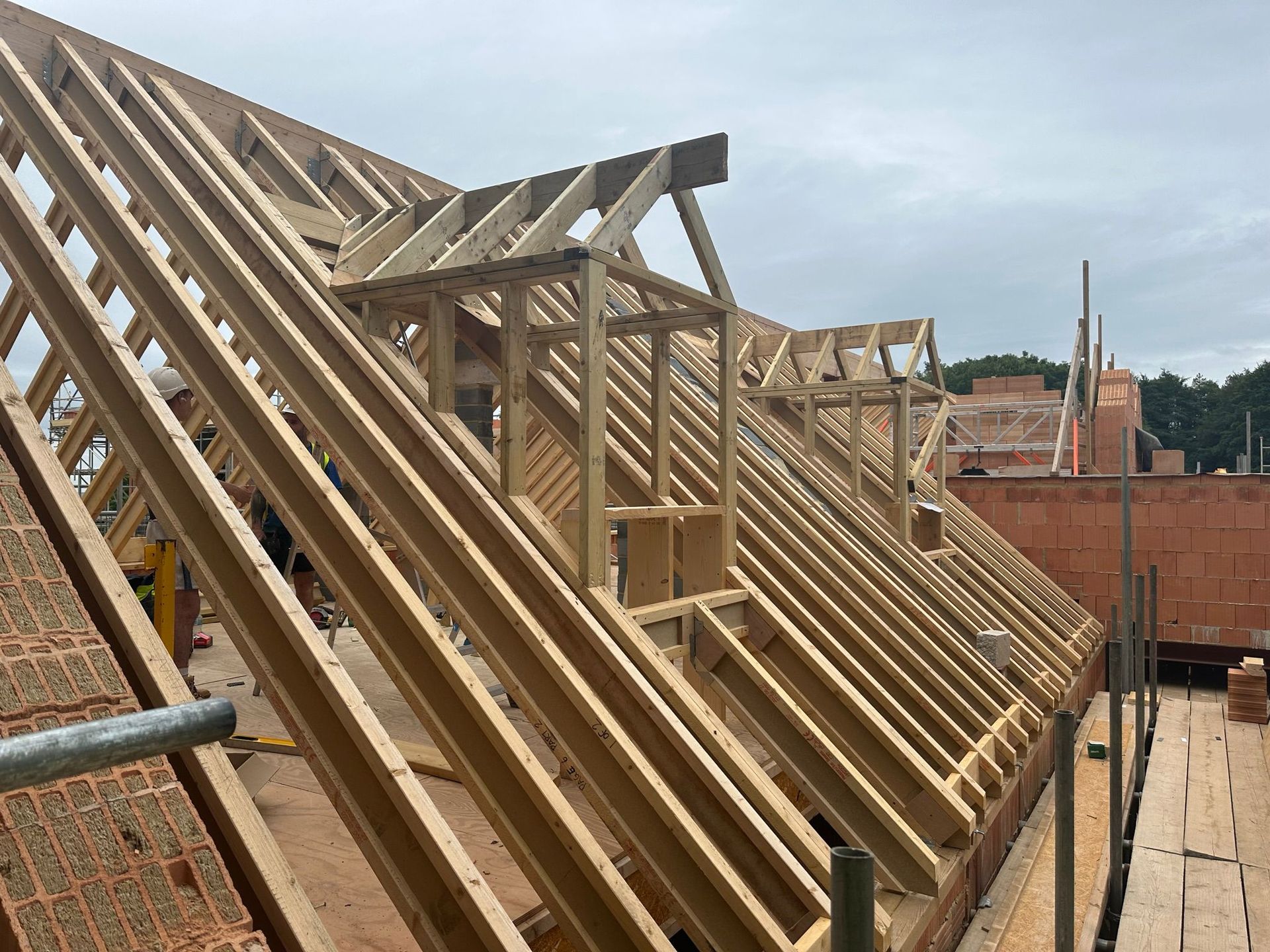 Wooden roof framing construction with a partially built dormer on a brick building.