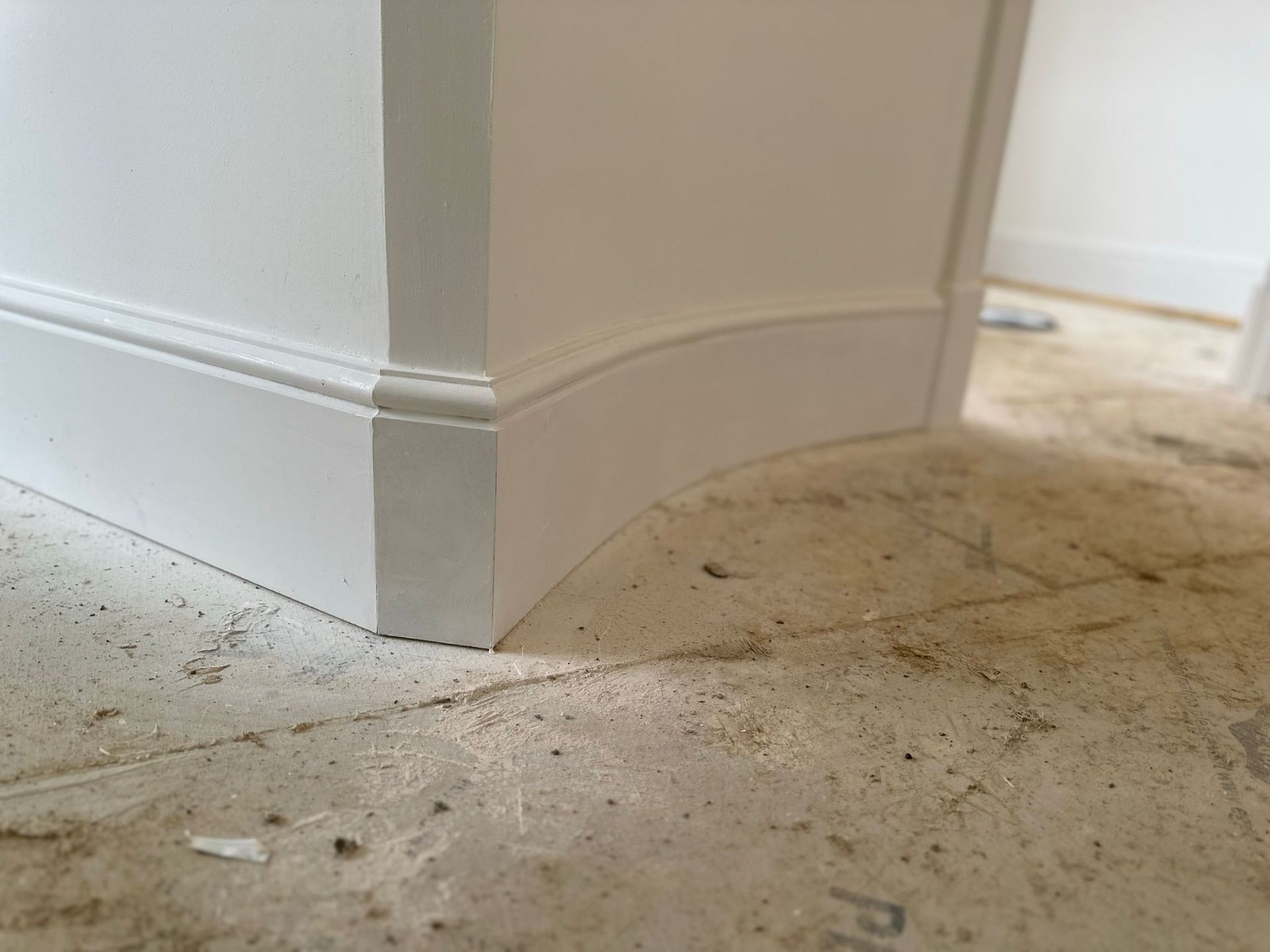 A person installing baseboard trim in a white room with a miter saw.