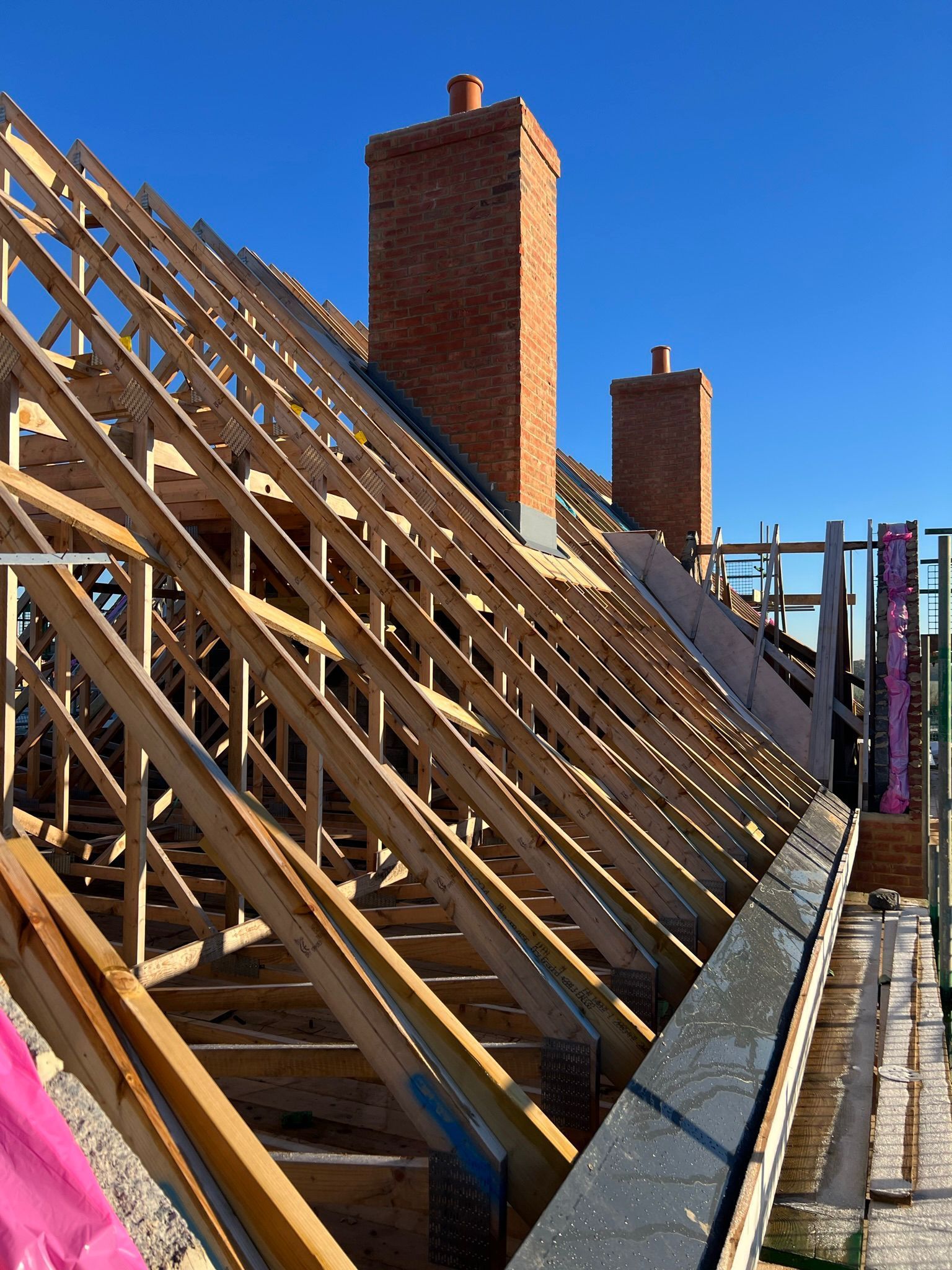 Wooden roof framing construction with a partially built dormer on a brick building.