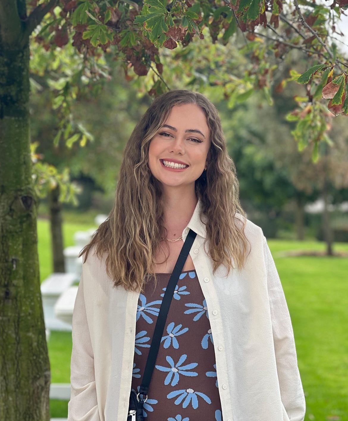 A woman is standing in front of a tree in a park and smiling.