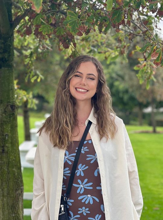 A woman is standing in front of a tree in a park and smiling.