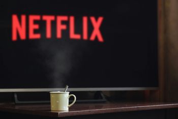 A cup of coffee sits in front of a netflix sign on a TV.
