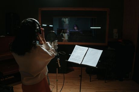 A woman is singing into a microphone in a recording studio.