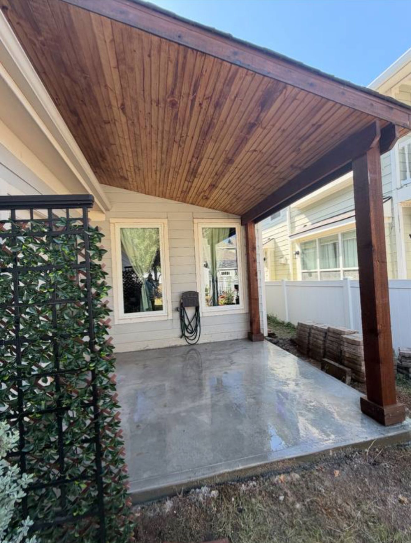 Covered patio with stained wood ceiling and support post, concrete floor, next to a house.