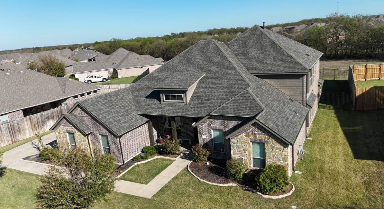 Aerial view of a suburban house with a gray roof, stone facade, and green lawn.