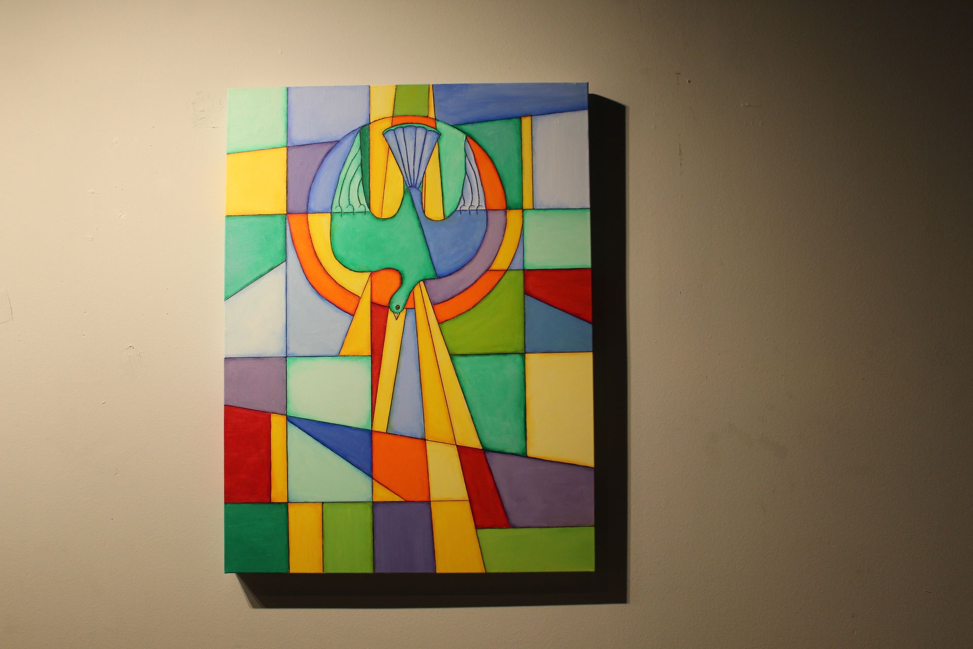 Colorful abstract artwork of a dove and rays of light, mounted on a wall.
