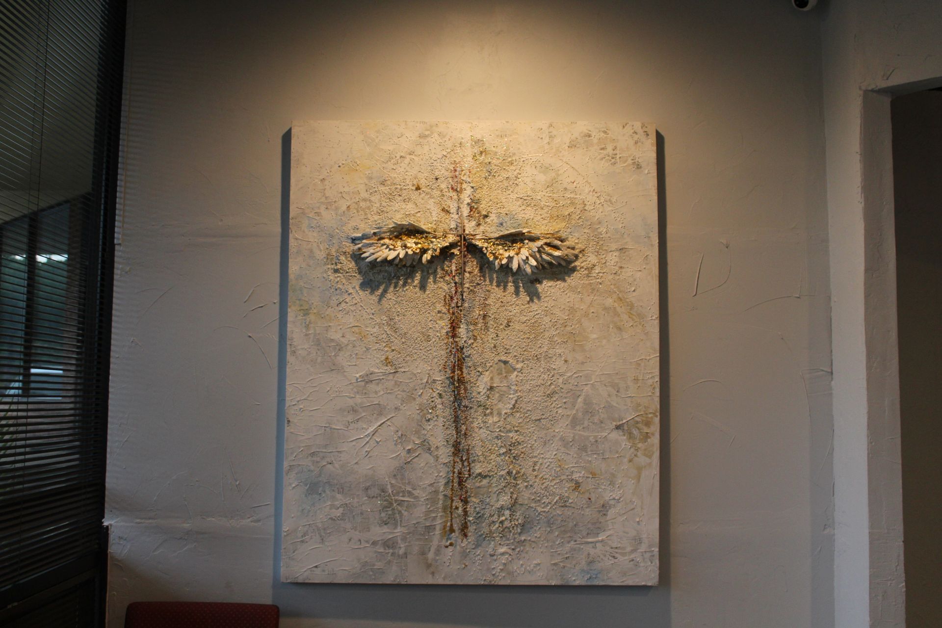 Textured abstract artwork on a wall. A vertical design with a central stem-like form and top branches. Light shines on it.