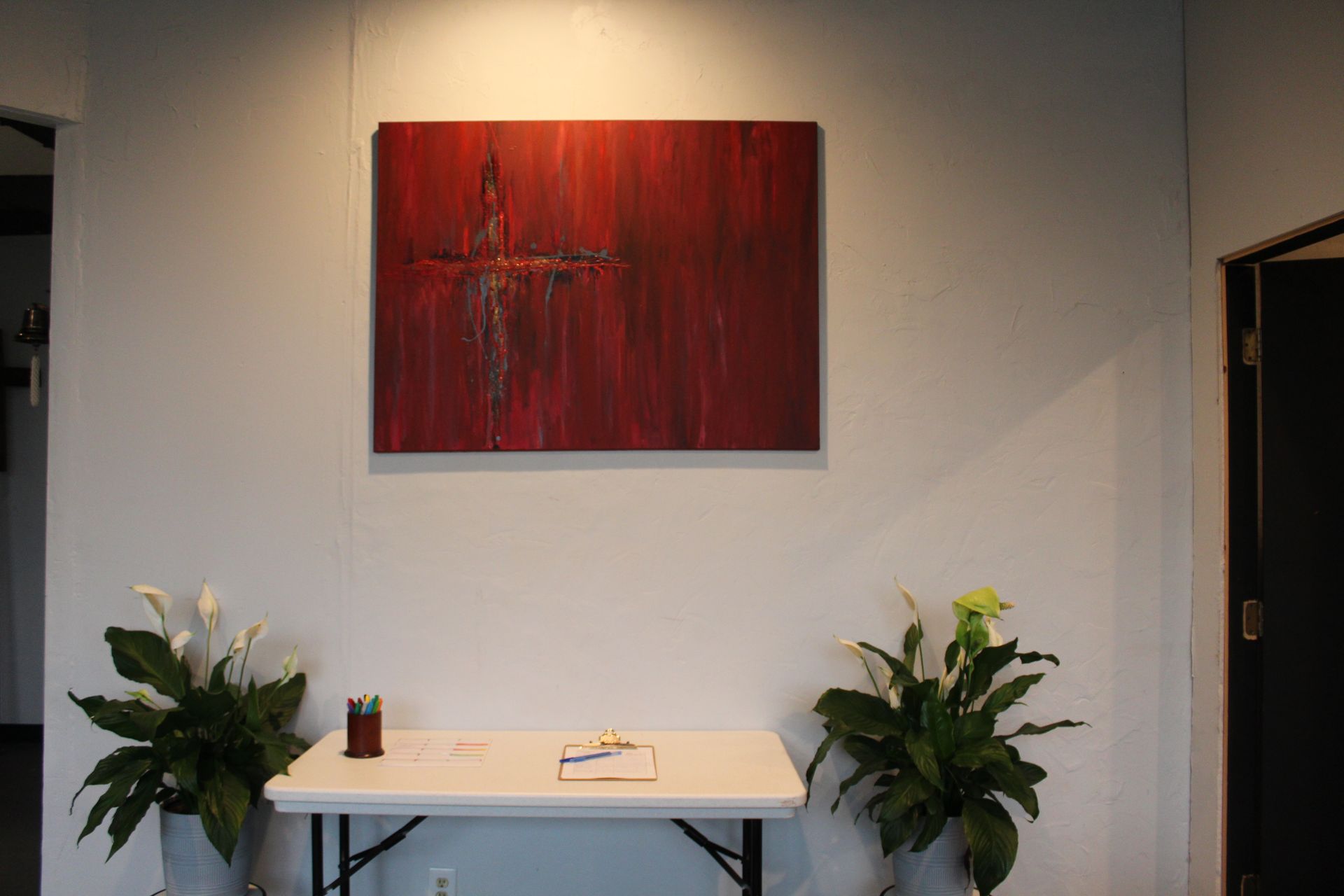 Red abstract painting on a white wall, above a white table with plants on either side.
