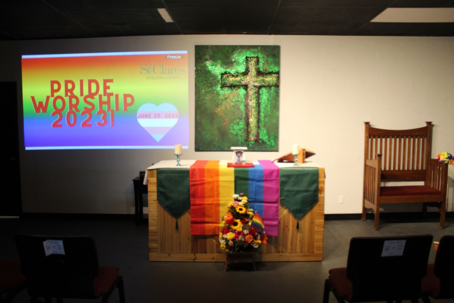 Altar with Pride flag colors, cross artwork, a projector screen reading 