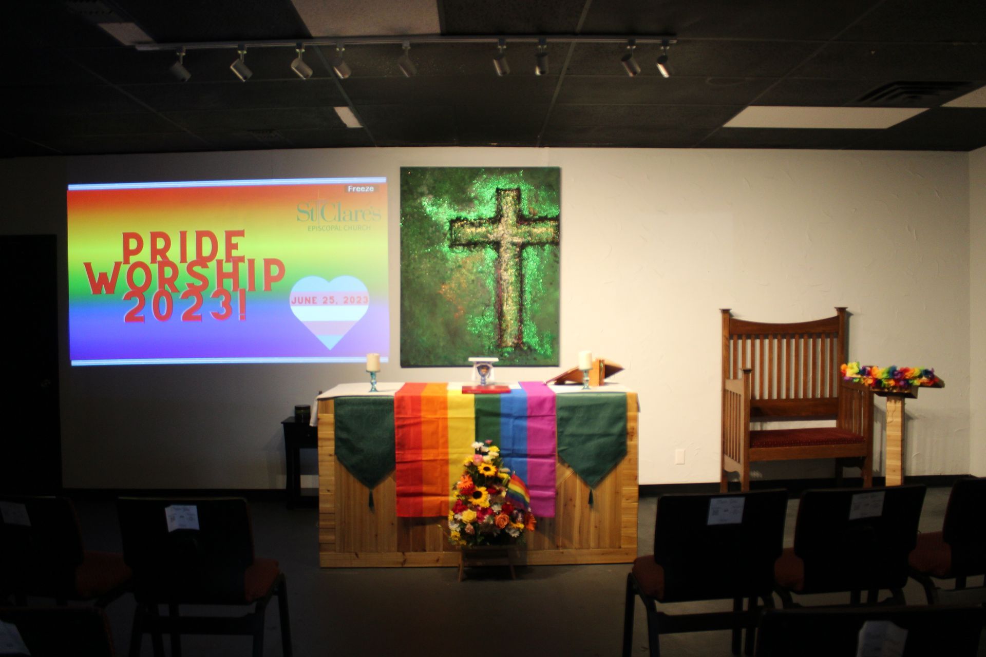 Interior of a church with a rainbow-colored Pride altar, a cross, and a Pride Worship 2023 projection.