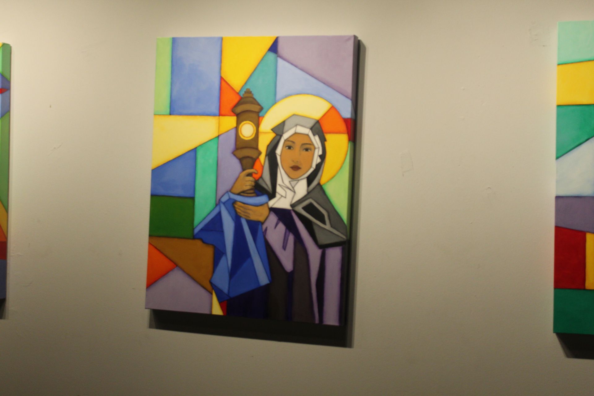 Painting of a figure in a nun's habit holding a lantern, geometric stained-glass style, mounted on a wall.