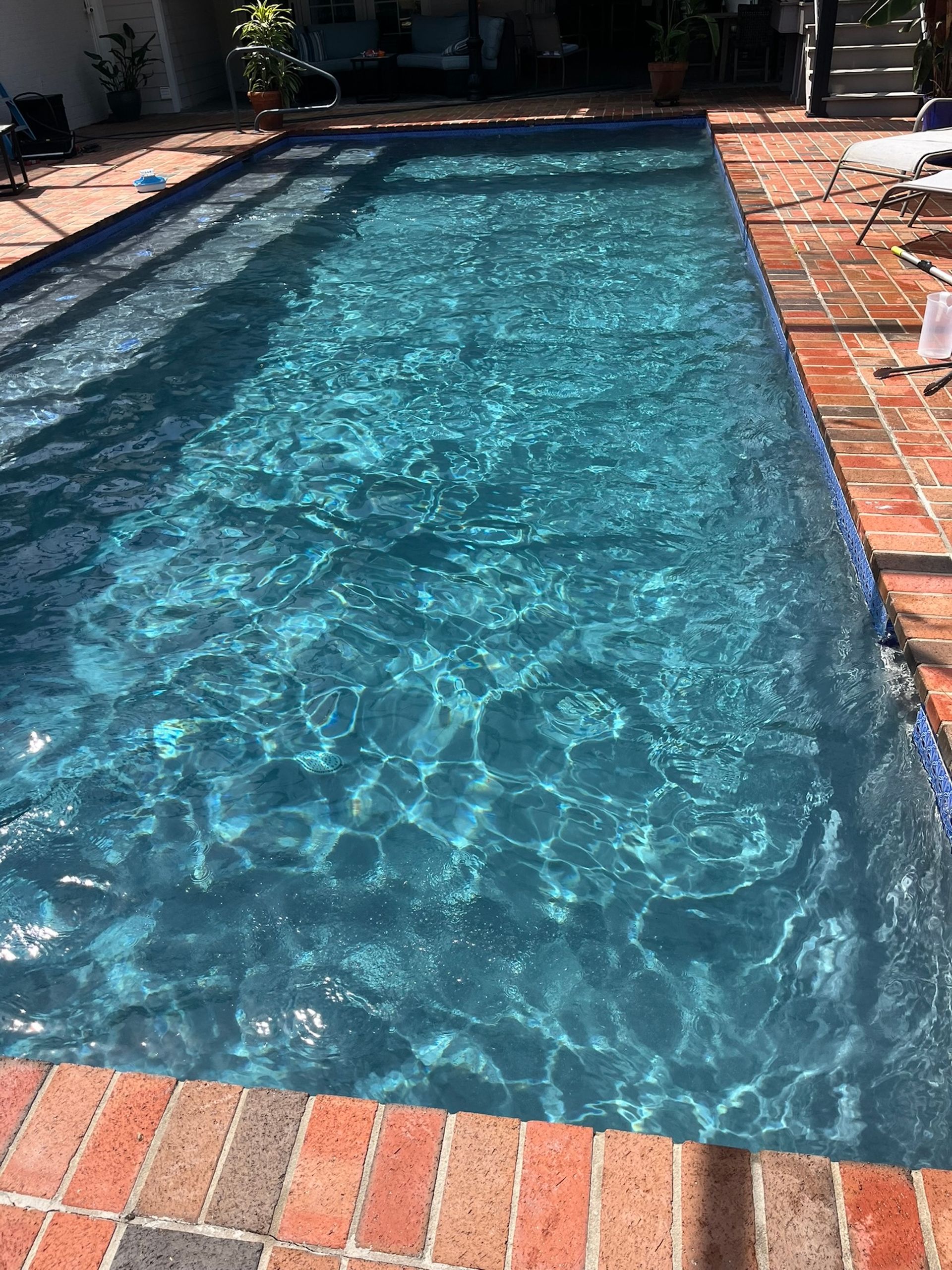 Rectangular pool with turquoise water, surrounded by red brick and blue tile.